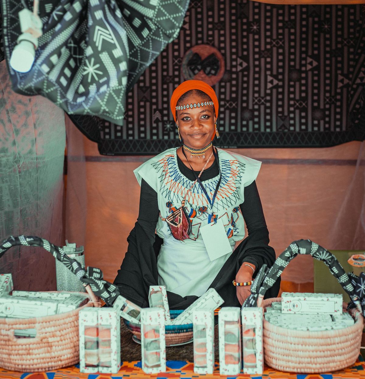 A smiling artisan in traditional attire at her market stall of handmade goods