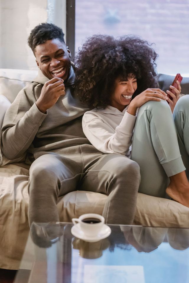 Un couple rit ensemble devant un téléphone sur son canapé