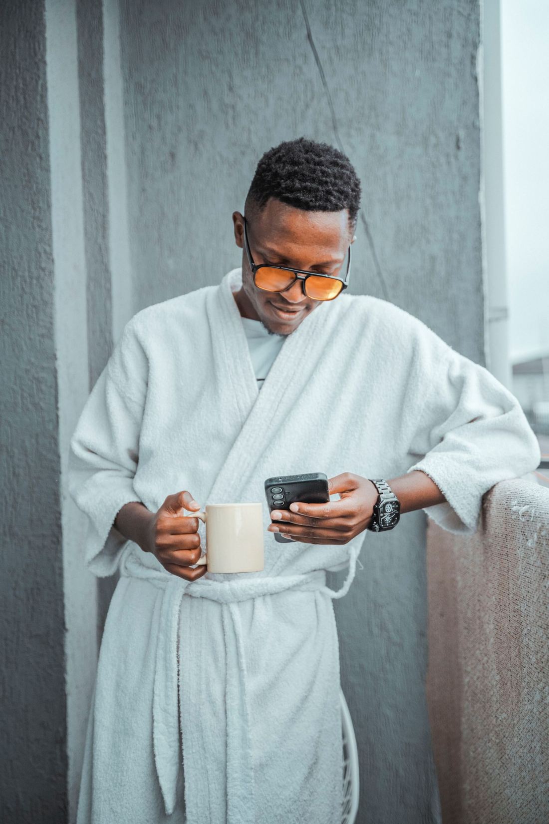 Un homme, café en main, lit son téléphone sur un balcon au-dessus de Nairobi