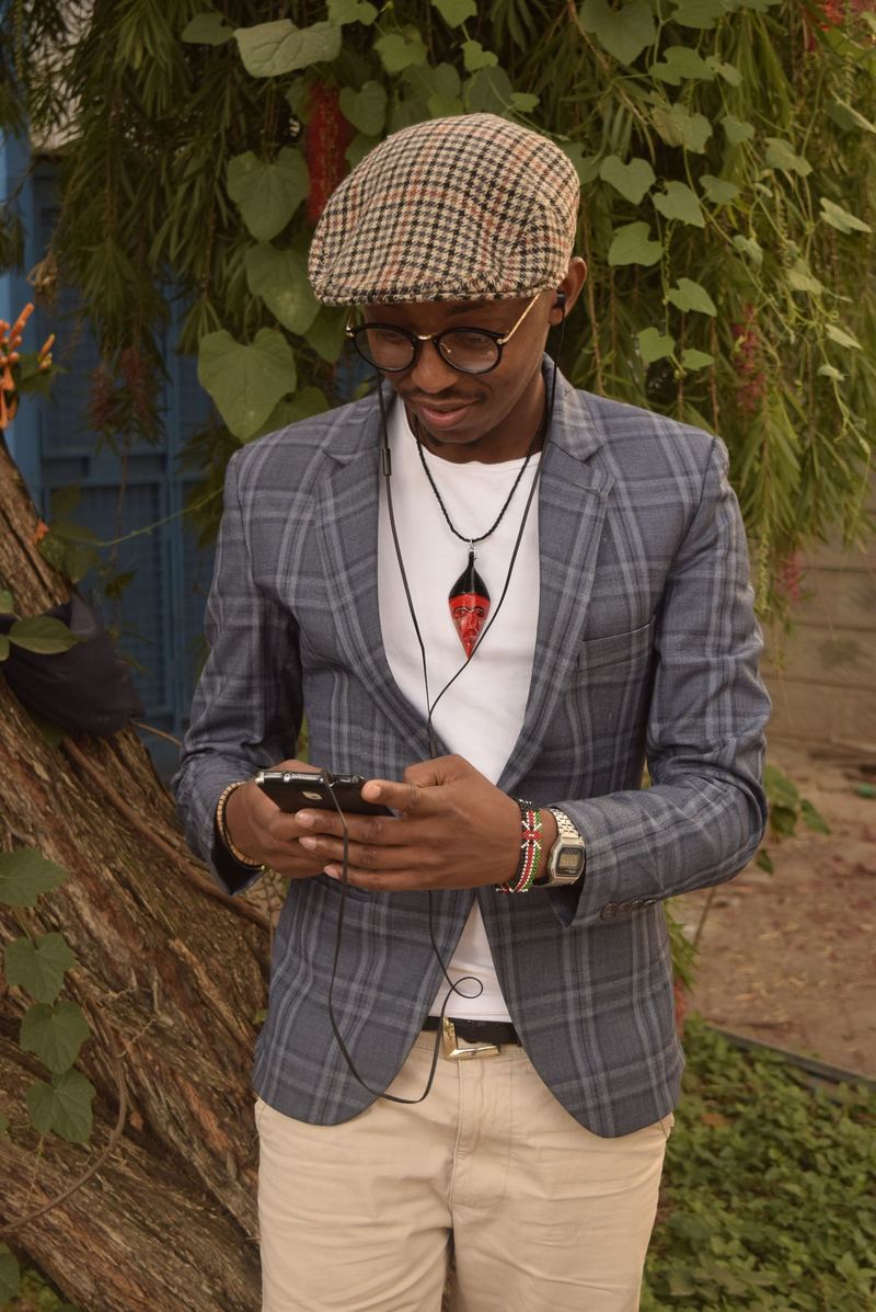 Un homme élégant lit son téléphone sous les arbres à Nairobi